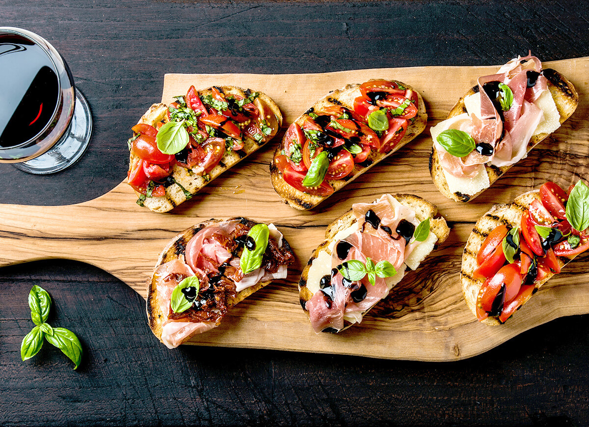Tapas españolas con jamón, tomate y albahaca sobre tabla de madera